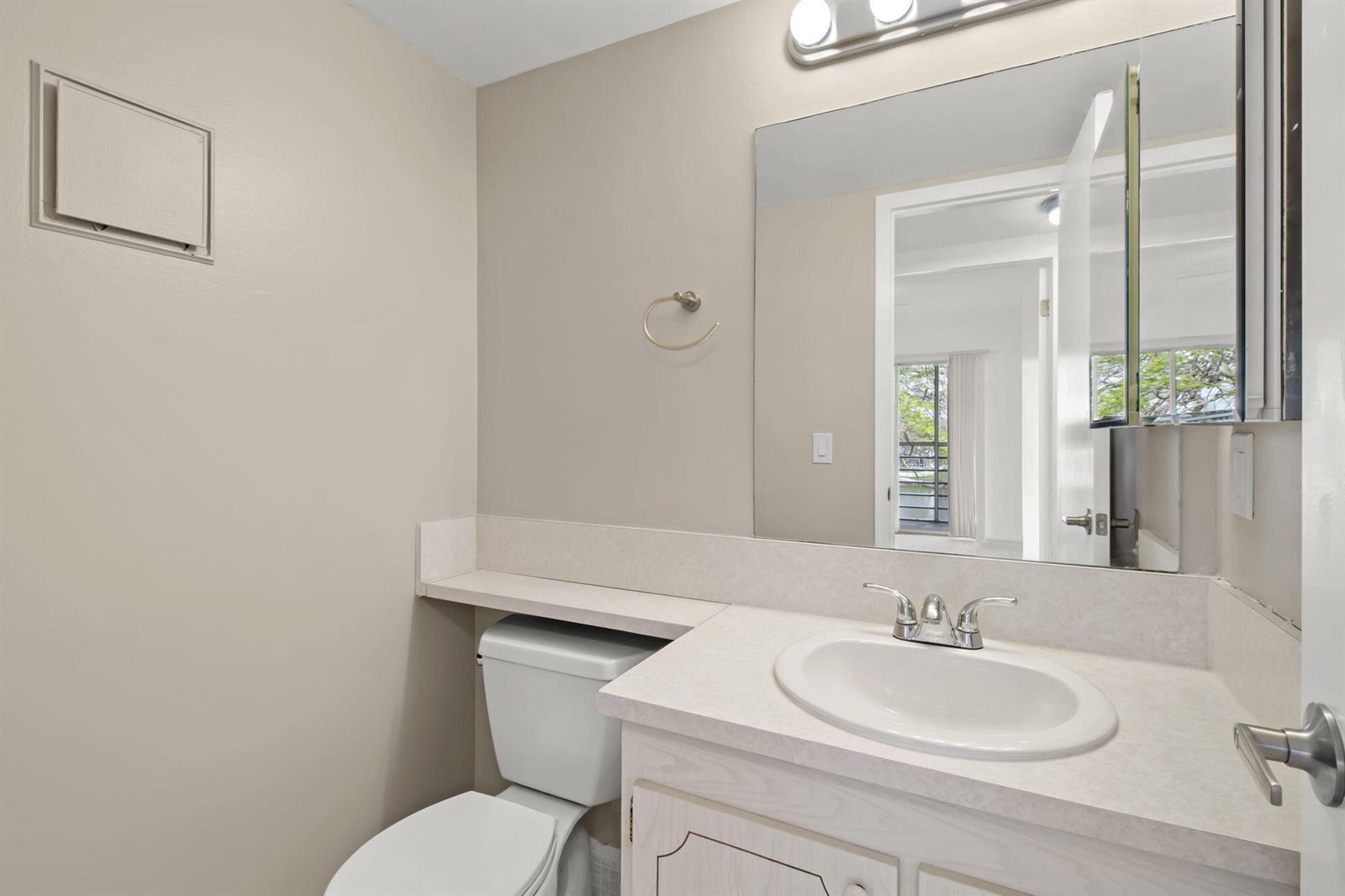 A bathroom features a vanity with a white sink, a toilet, and a wall mirror — 124 Preston C, Boca Raton FL 33434, BOCA RATON, FL