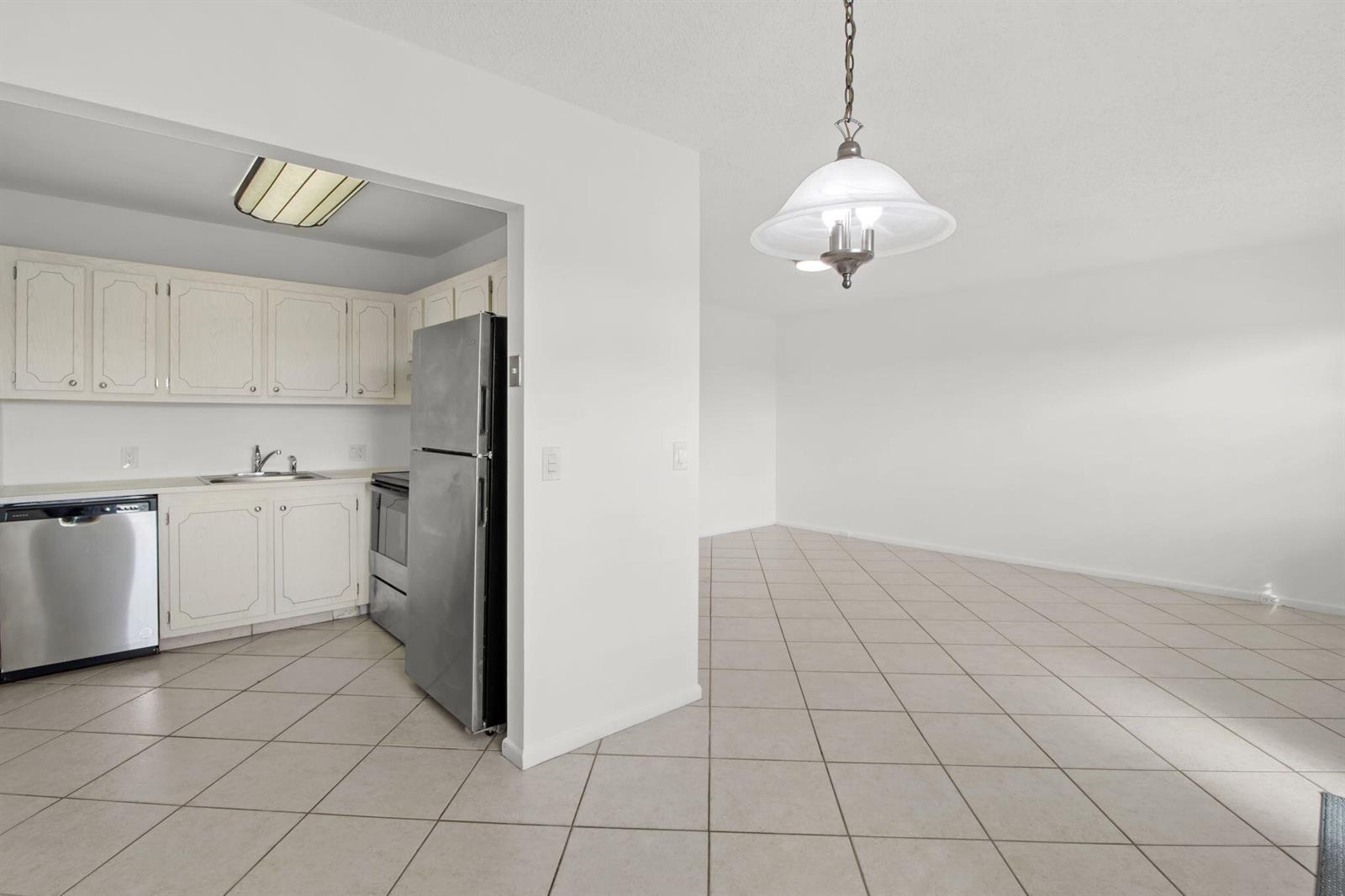 A kitchen with white cabinets and stainless steel appliances opens to a tiled dining area — 124 Preston C, Boca Raton FL 33434, BOCA RATON, FL
