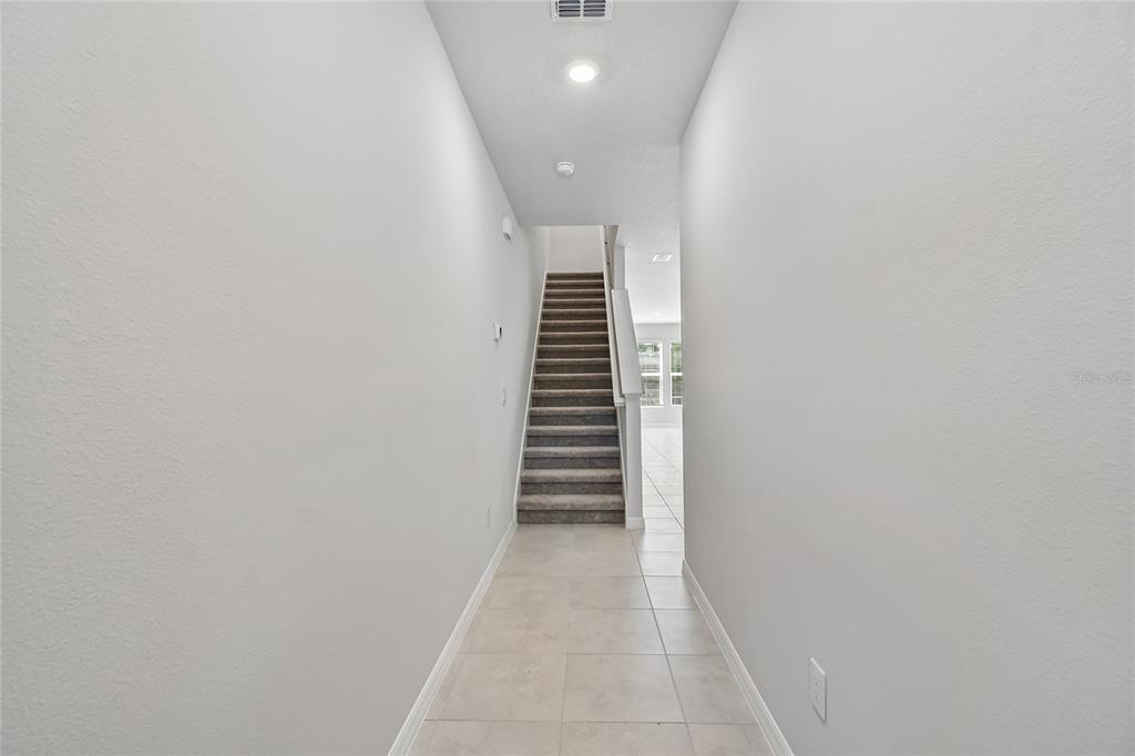 A tiled hallway leads to a carpeted staircase in a home with white walls — 1124 WILD CREST LANE, DAYTONA BEACH, FL
