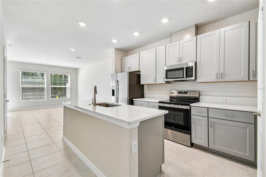 A kitchen with light gray cabinets, white countertops, and a central island overlooks a living area — 1124 WILD CREST LANE, DAYTONA BEACH, FL