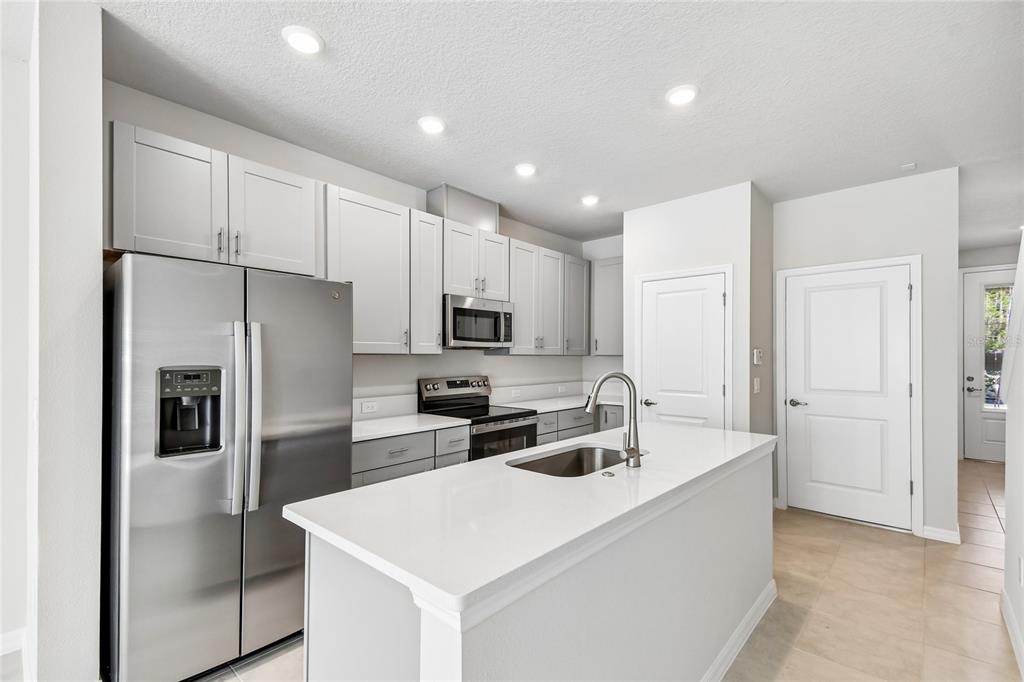 A modern kitchen features light gray cabinets, stainless steel appliances, and a white quartz island — 1124 WILD CREST LANE, DAYTONA BEACH, FL