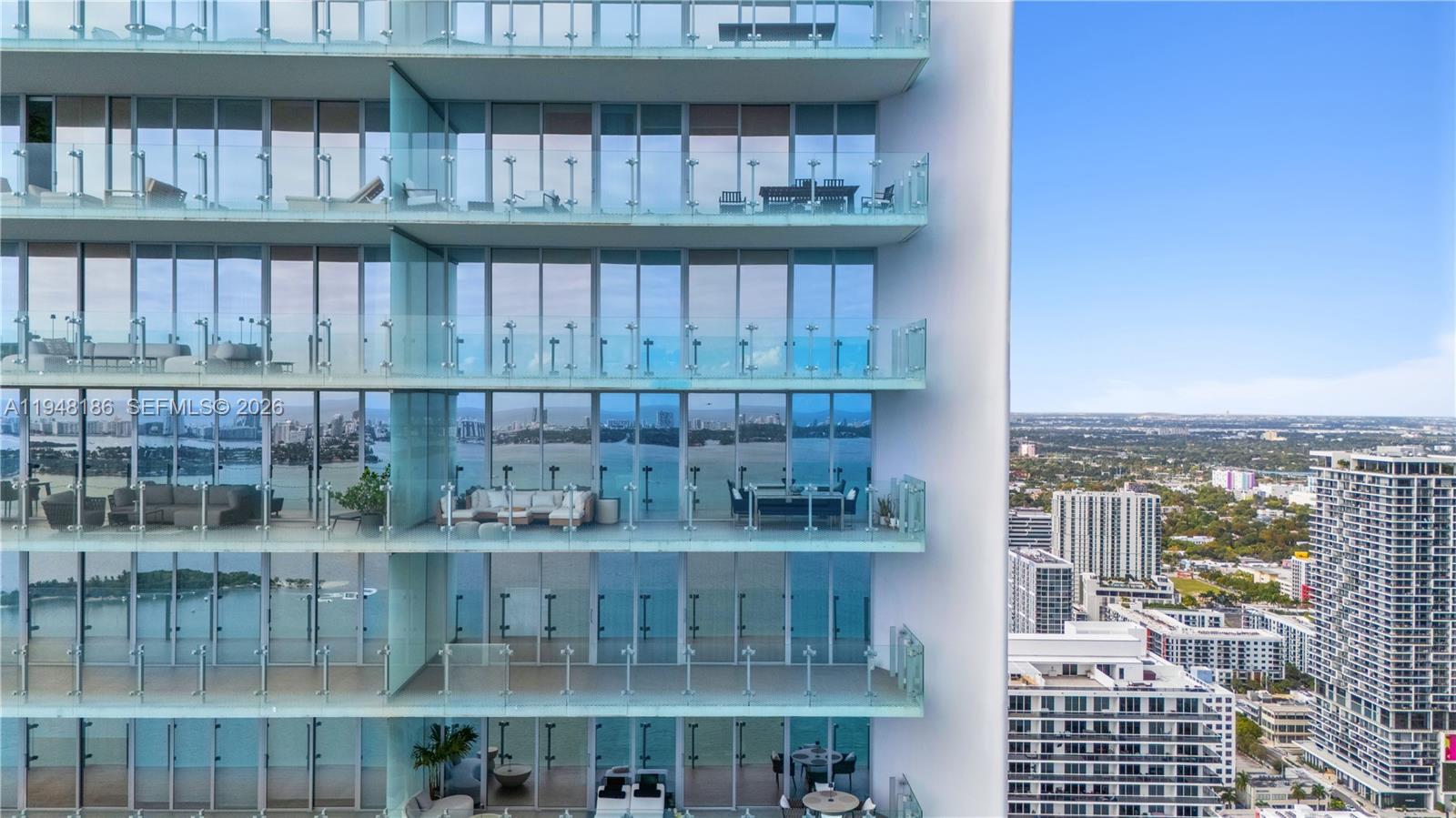 A high-rise building features multiple stacked balconies with glass railings overlooking a bay — 700 NE 26th Ter # 4701, Miami FL 33137, MIAMI, FL