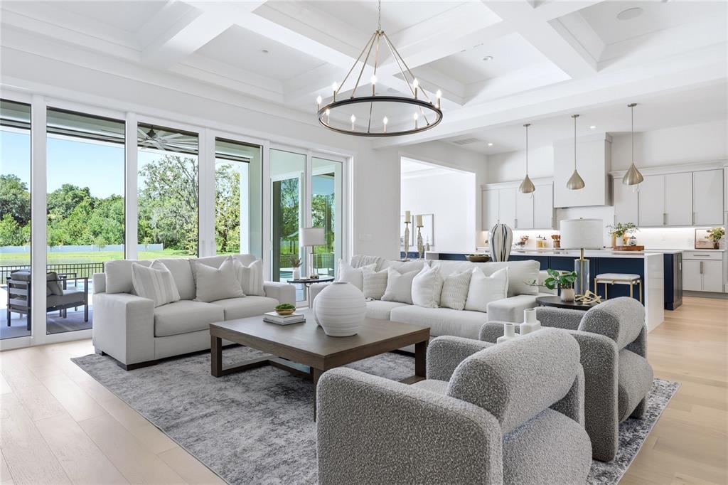 A bright, open-concept living room features a coffered ceiling, modern chandelier, and sliding glass doors — 1134 PRADO LANE, OAKLAND, FL