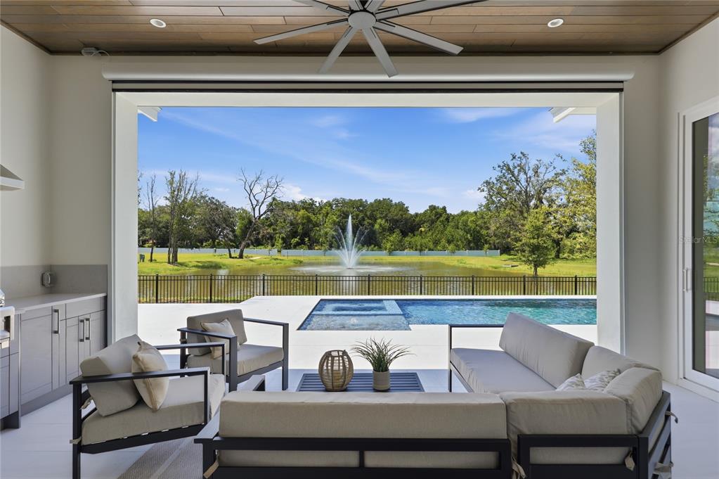 A covered patio with outdoor seating overlooks a swimming pool and a pond with a fountain — 1134 PRADO LANE, OAKLAND, FL