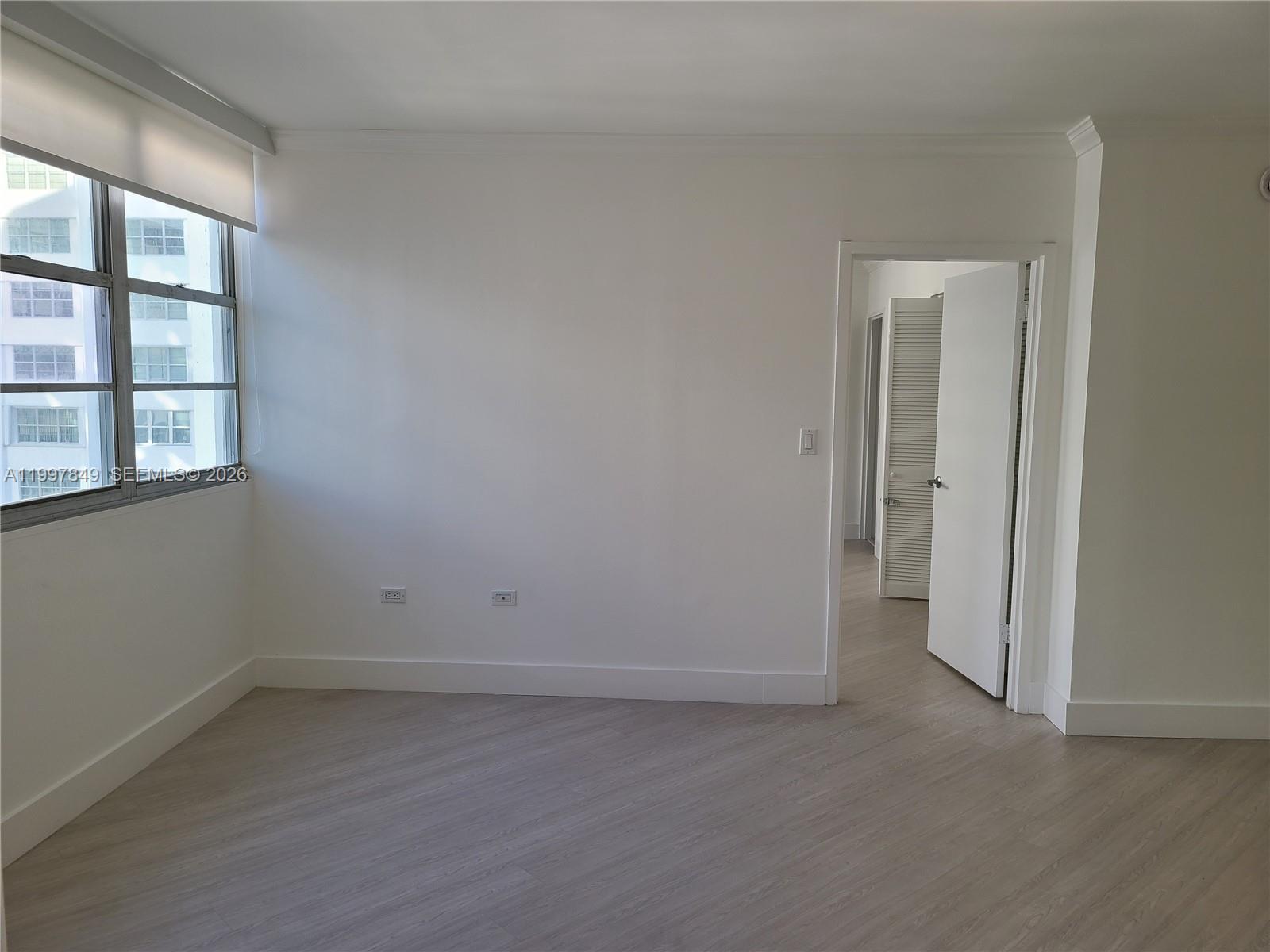 An empty room features white walls, light-colored wood-look flooring, and a window with a shade — 999 Brickell Bay Dr # 1207, Miami FL 33131, MIAMI, FL