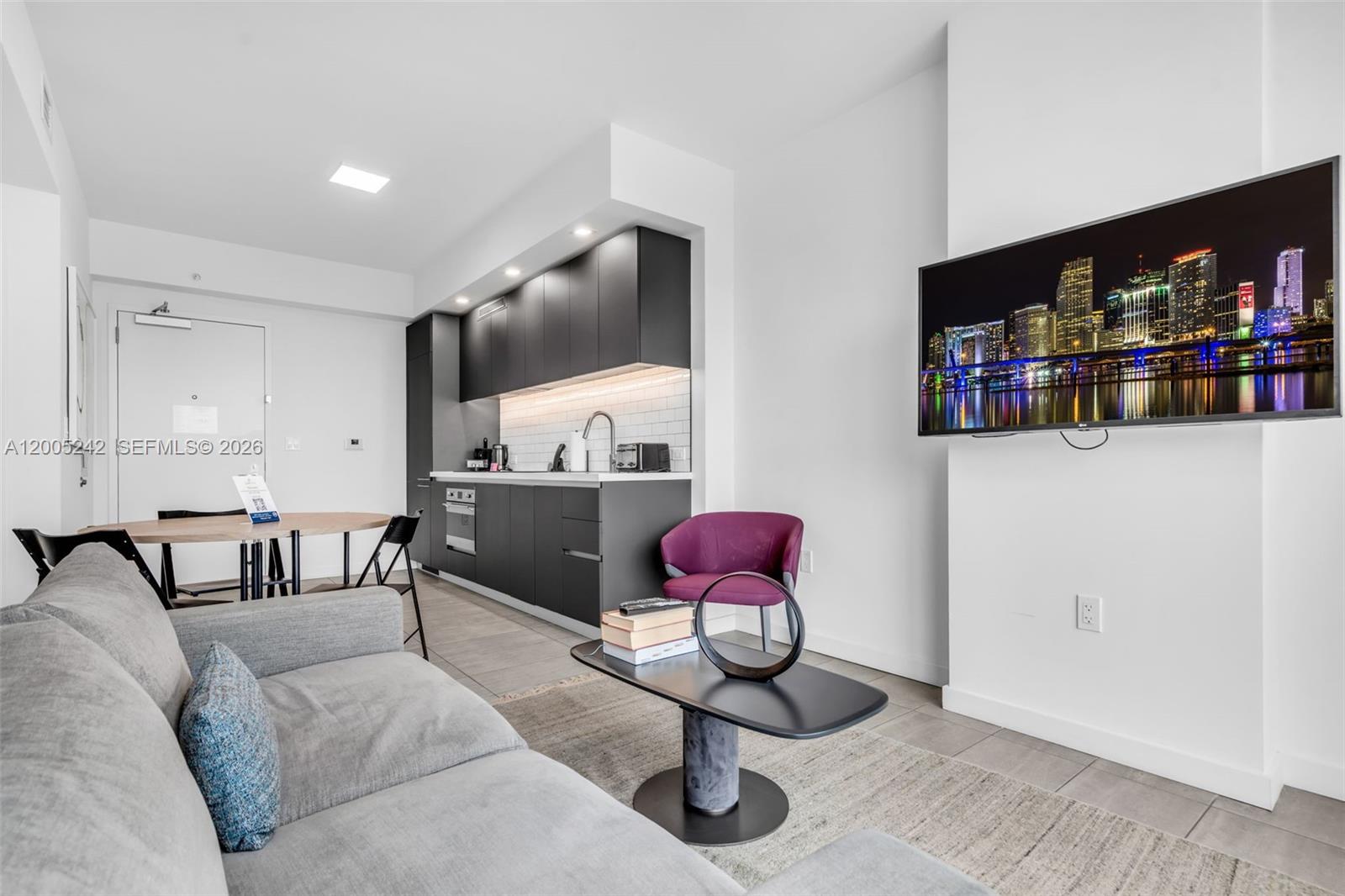 A modern studio apartment features a gray sofa, a small dining table, and a kitchenette — 227 NE 2nd St # 2503, Miami FL 33132, MIAMI, FL