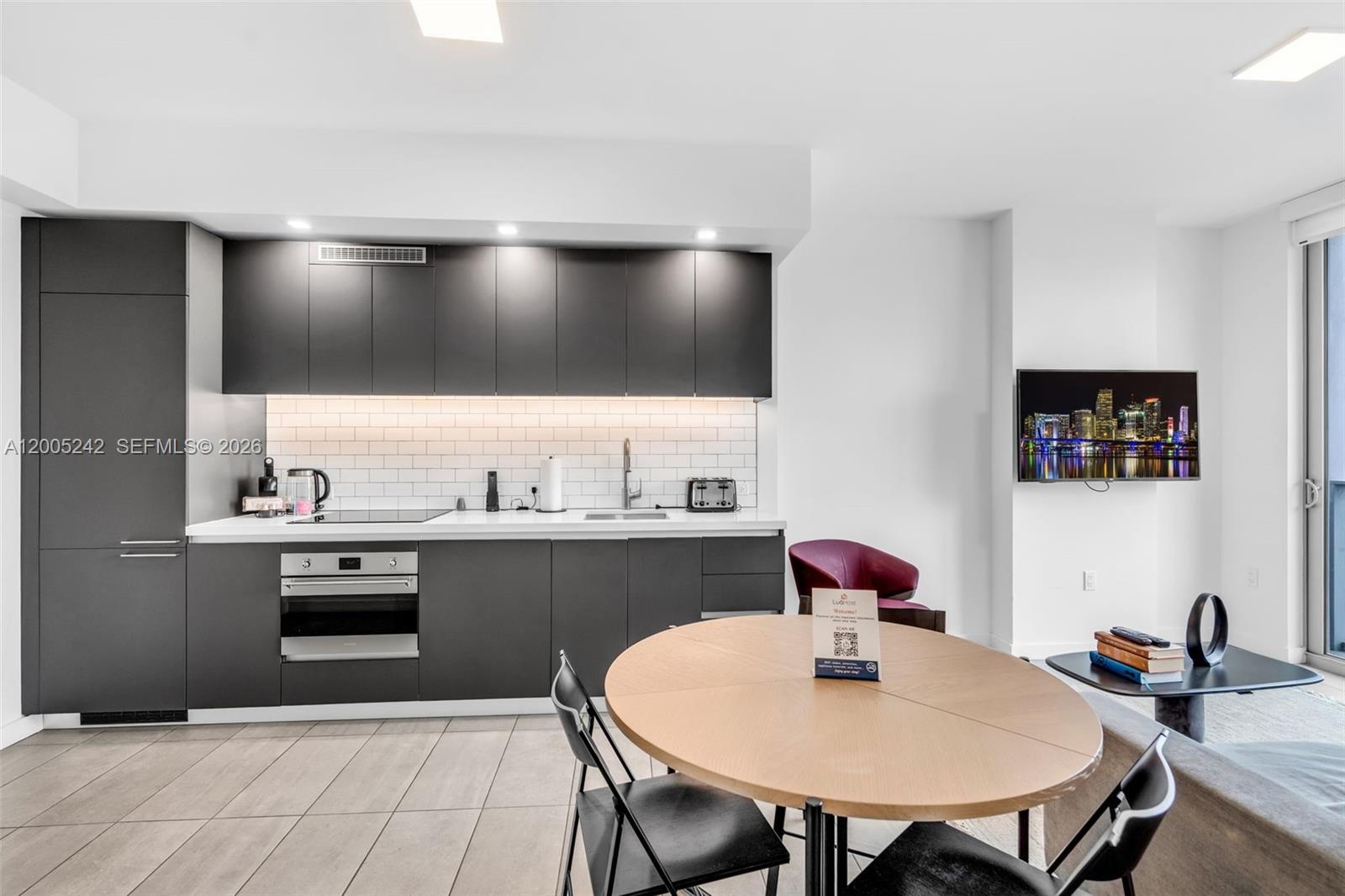 A modern kitchen features dark cabinetry, white subway tile backsplash, and a round dining table — 227 NE 2nd St # 2503, Miami FL 33132, MIAMI, FL