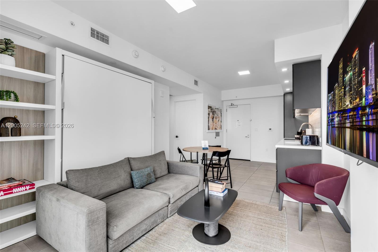 A studio apartment features a grey sofa, a dining table, a kitchenette, and a wall bed — 227 NE 2nd St # 2503, Miami FL 33132, MIAMI, FL