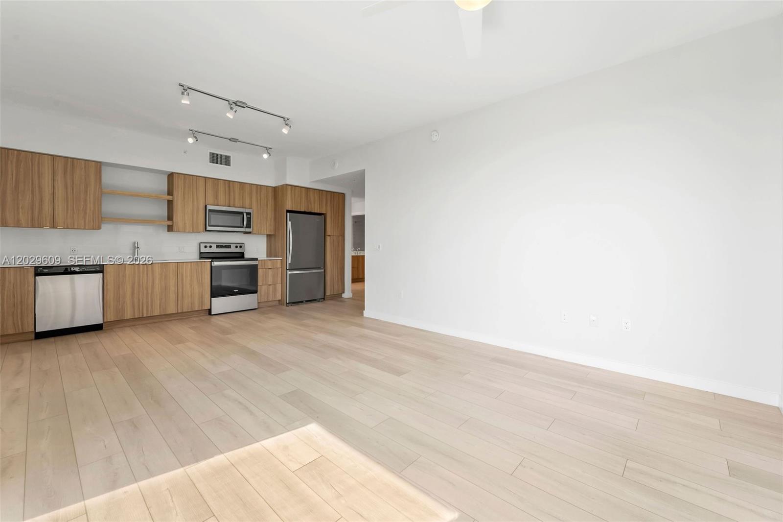 A modern kitchen with light wood cabinets and stainless steel appliances opens into a living area — FORT LAUDERDALE, FL