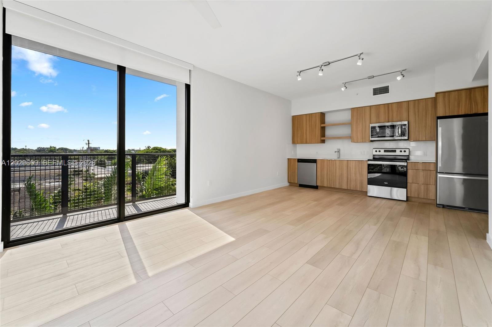A modern kitchen with light wood cabinets and stainless steel appliances opens to a balcony — FORT LAUDERDALE, FL