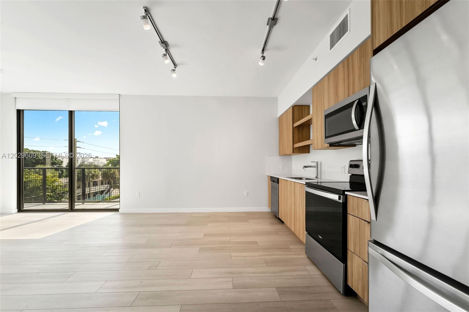 A modern kitchen with light wood cabinets and stainless steel appliances opens to a balcony — FORT LAUDERDALE, FL