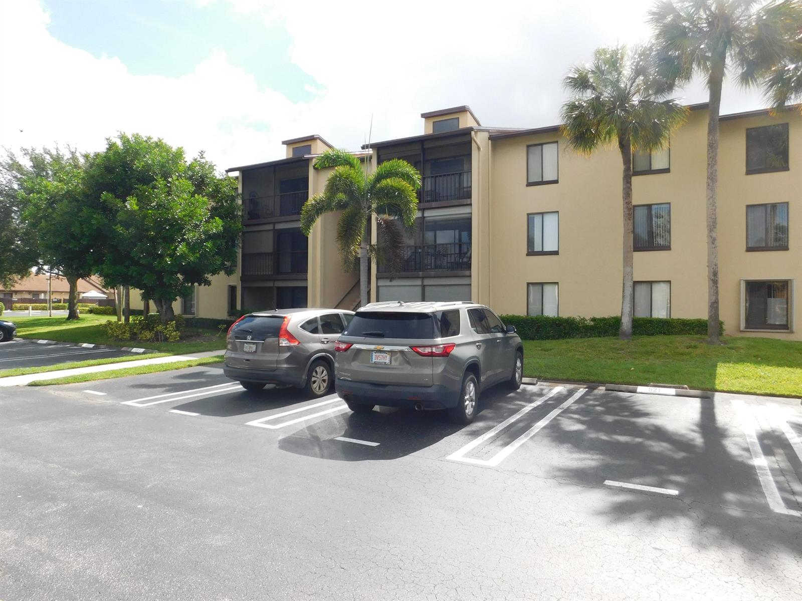 A three-story apartment building with tan stucco walls stands behind a paved parking lot — 627 Sea Pine Way # A2, FL 33415, FL