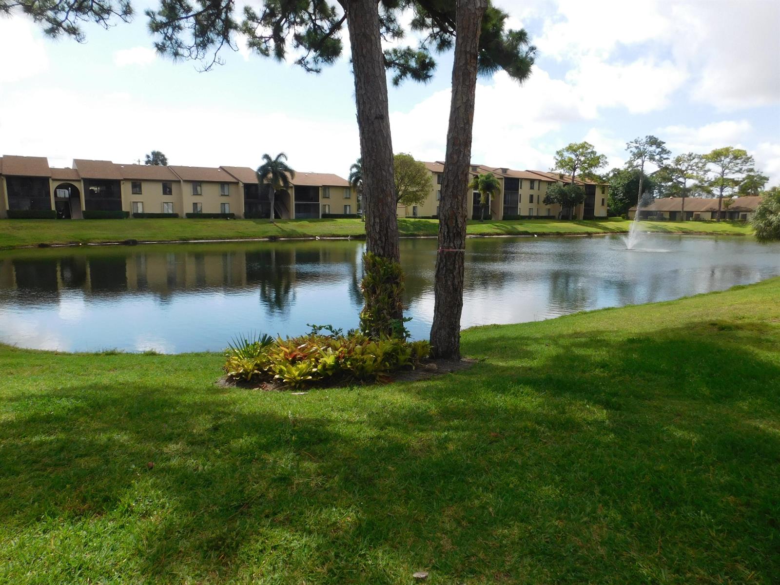 A pond with a fountain sits in front of apartment buildings and two pine trees — 627 Sea Pine Way # A2, FL 33415, FL