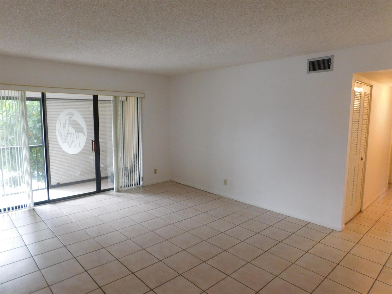 An empty living room features beige tile flooring, white walls, and a sliding glass door — 627 Sea Pine Way # A2, FL 33415, FL