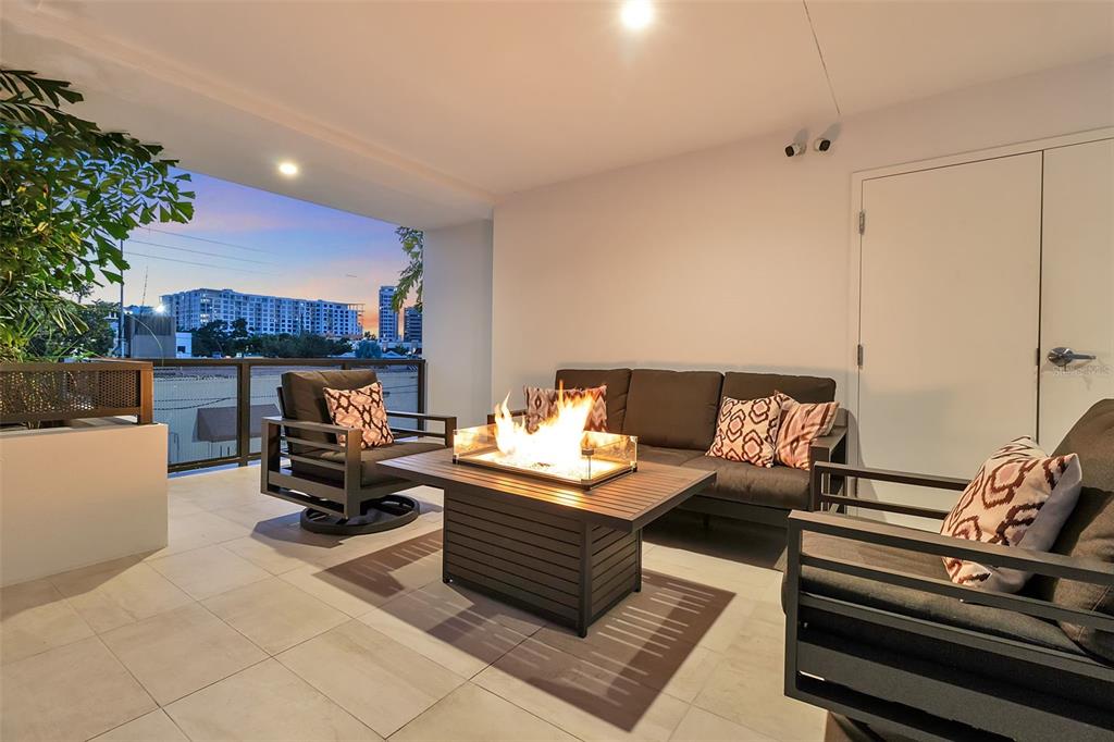 A modern outdoor balcony features a fire pit table, lounge seating, and city skyline views — 1542 4TH STREET UNIT 210, SARASOTA, FL