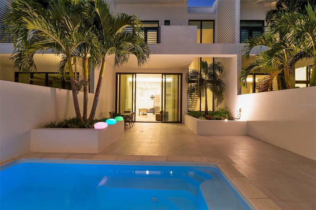 A modern patio with a swimming pool, palm trees, and glowing lights at dusk — 1542 4TH STREET UNIT 210, SARASOTA, FL
