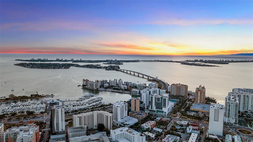 An aerial view shows a coastal city skyline, a bridge, and a marina at sunset — 1542 4TH STREET UNIT 210, SARASOTA, FL