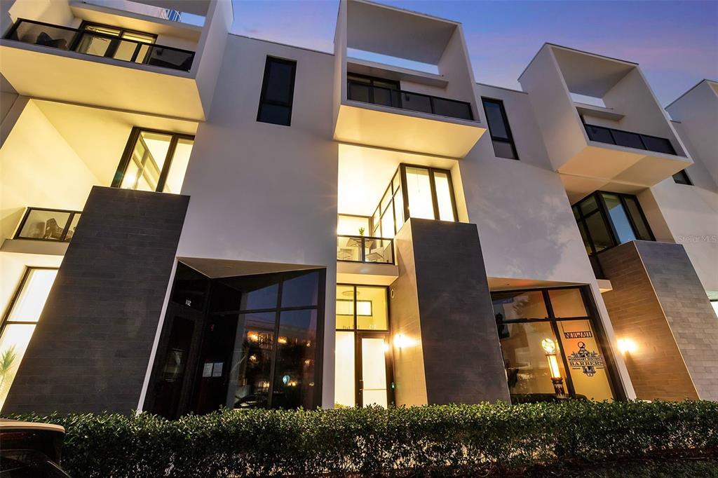 A modern multi-story building exterior features white geometric balconies, dark stone accents, and glass storefronts — 1542 4TH STREET UNIT 210, SARASOTA, FL
