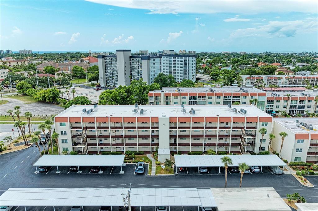 An aerial view of a multi-story apartment building with covered parking spaces in the foreground — 220 SANTA MARIA STREET UNIT 338, VENICE, FL