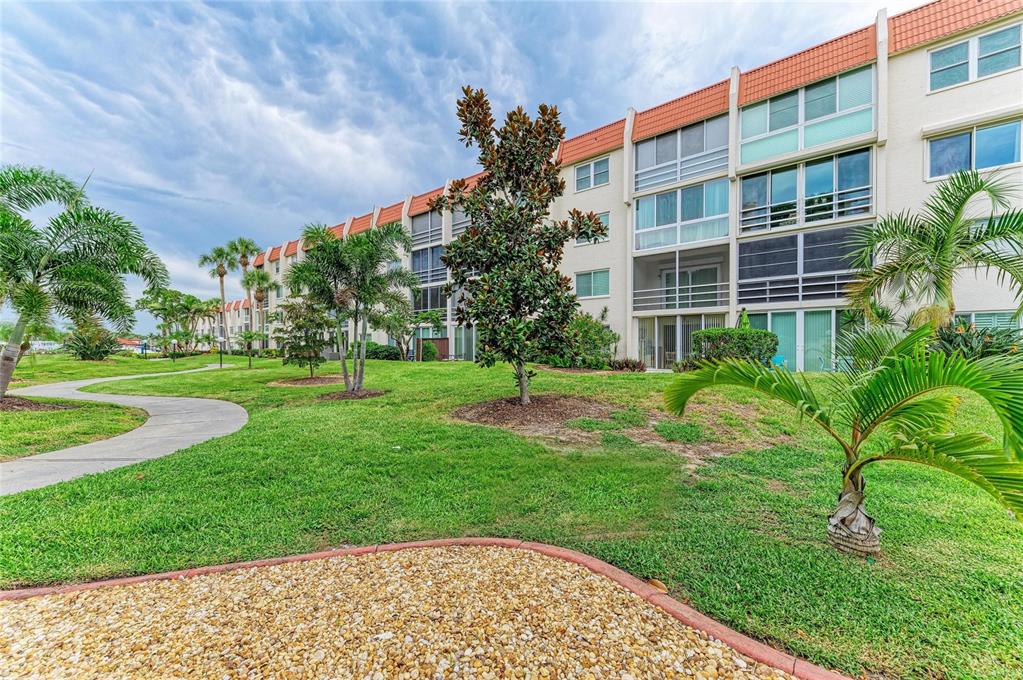 A multi-story apartment building with balconies stands behind a grassy lawn and a walking path — 220 SANTA MARIA STREET UNIT 338, VENICE, FL