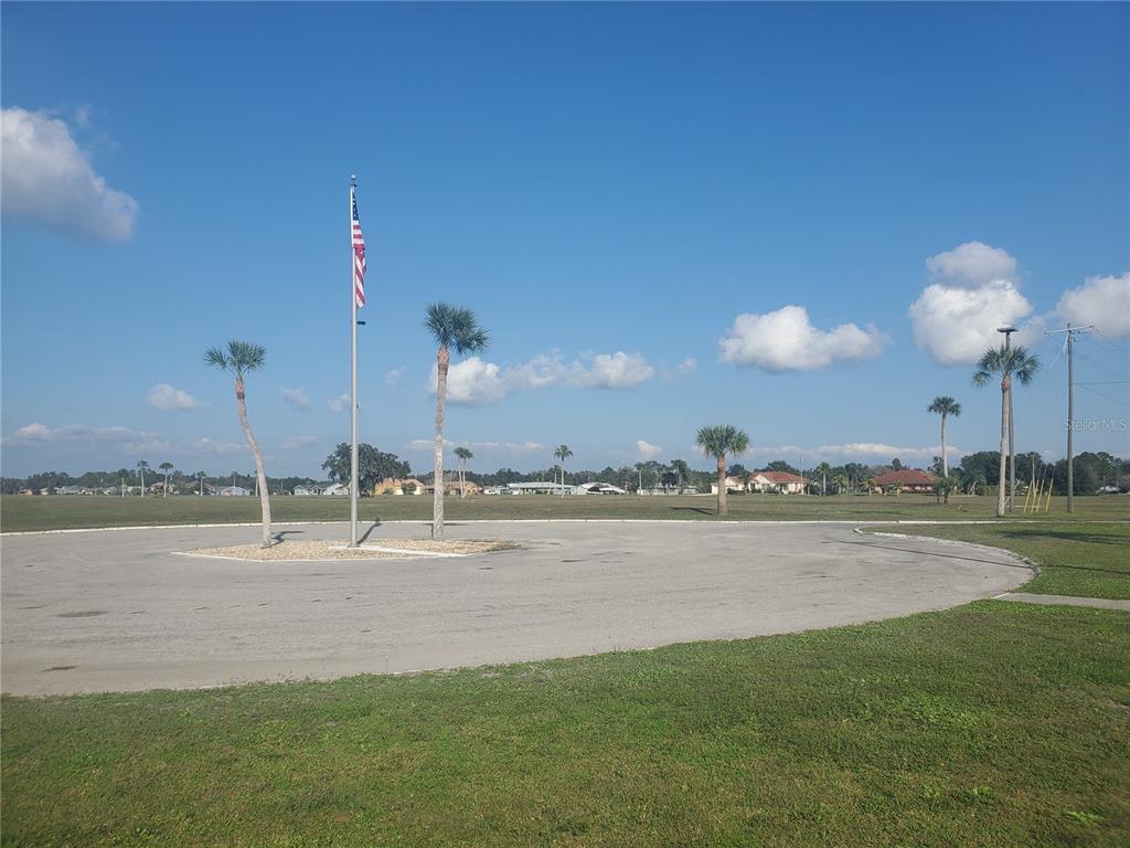 A paved circular driveway features a flagpole and palm trees against a clear blue sky — 715 INDIAN LAKE DRIVE, INDIAN LAKE ESTATES, FL