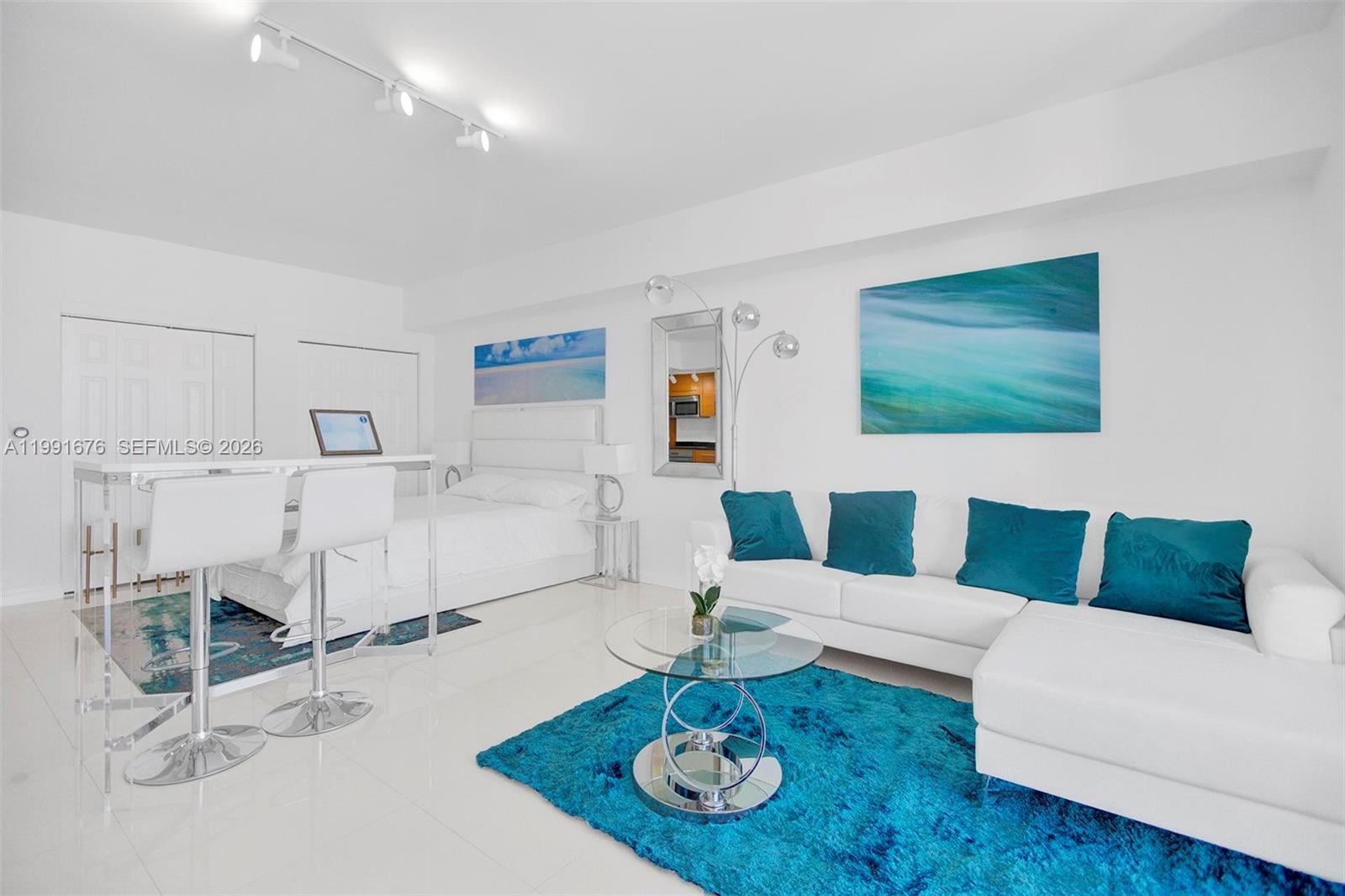 A modern studio apartment features a white sofa, a bed, and blue accent decor — 475 Brickell Ave # 5010, Miami FL 33131, MIAMI, FL