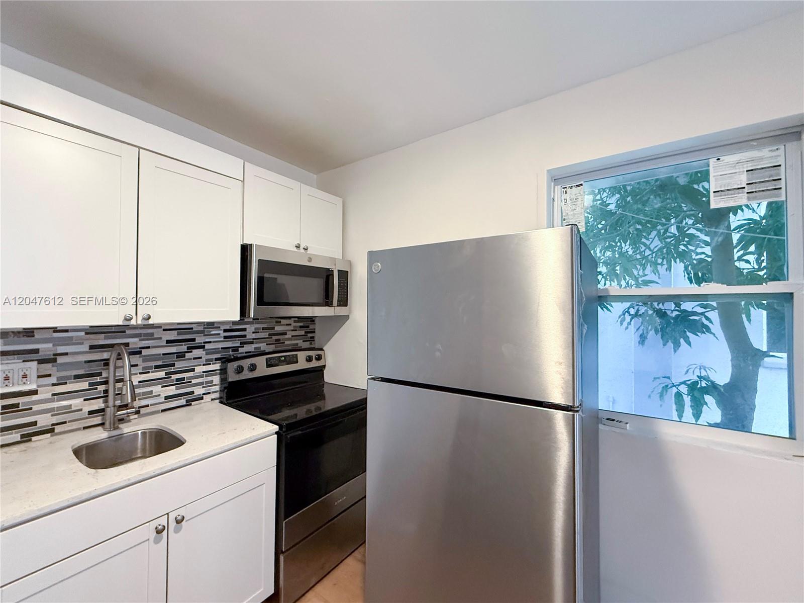 A kitchen features white cabinets, stainless steel appliances, a tiled backsplash, and a window — 2 SW 6th Ave # 4, Dania Beach FL 33004, DANIA BEACH, FL