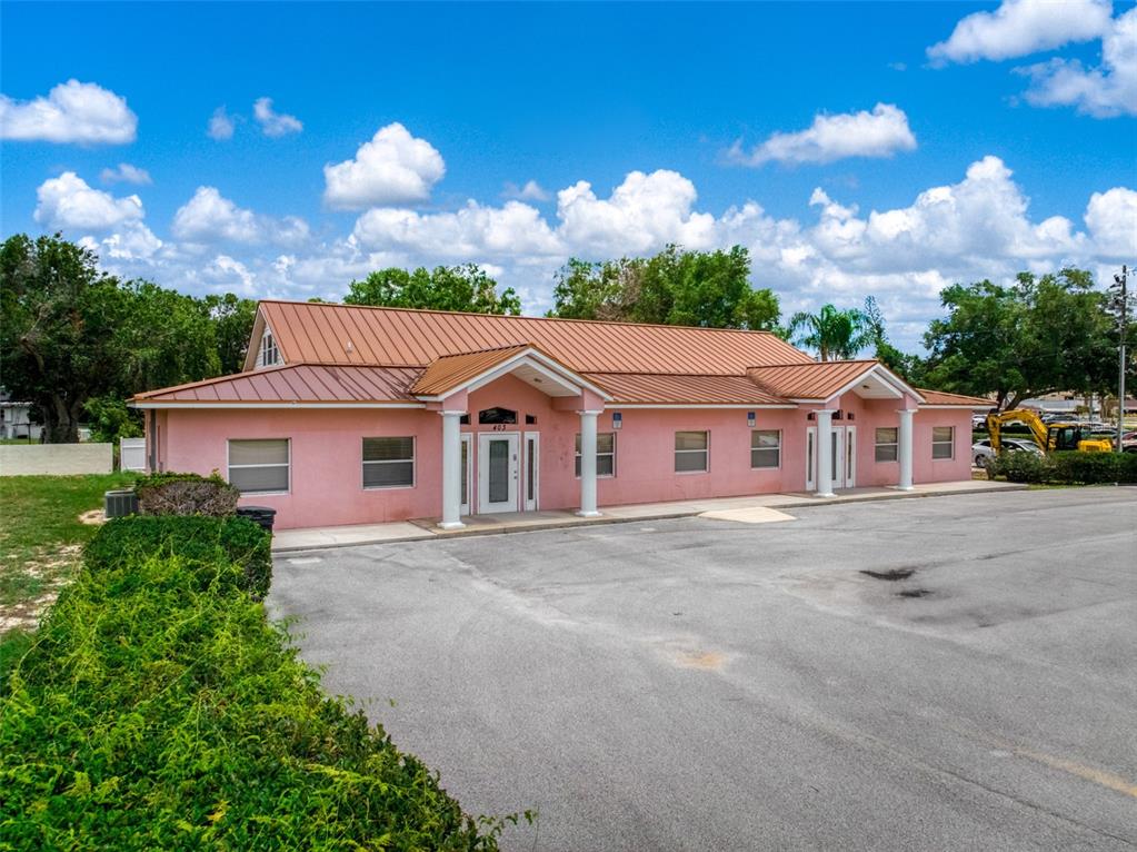 A pink commercial building with a metal roof and two columned entrances faces a parking lot — 401 W INTERLAKE BOULEVARD, LAKE PLACID, FL