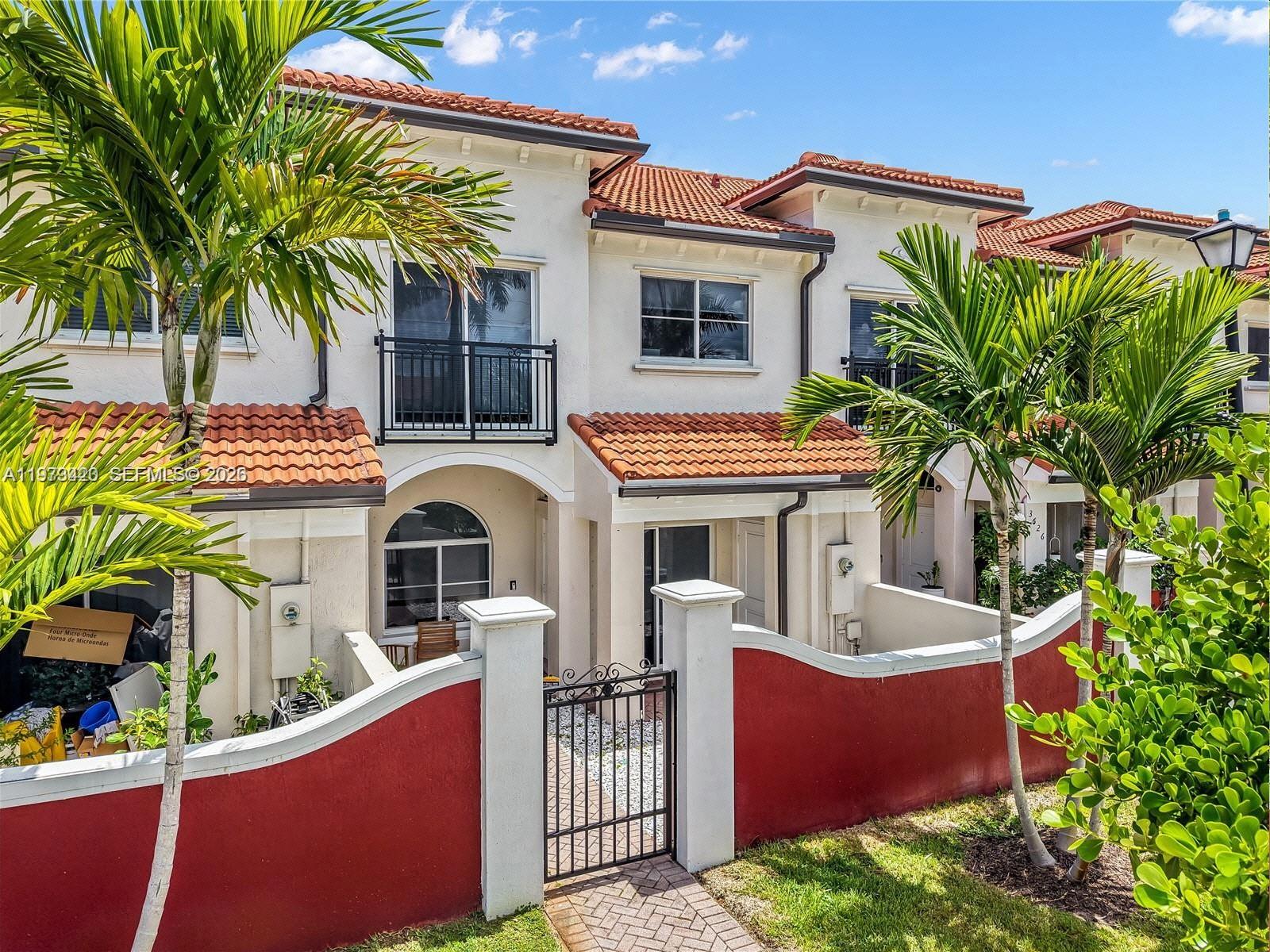 A two-story townhouse exterior features a red-painted courtyard wall, palm trees, and tiled roofing — LAUDERDALE LAKES, FL