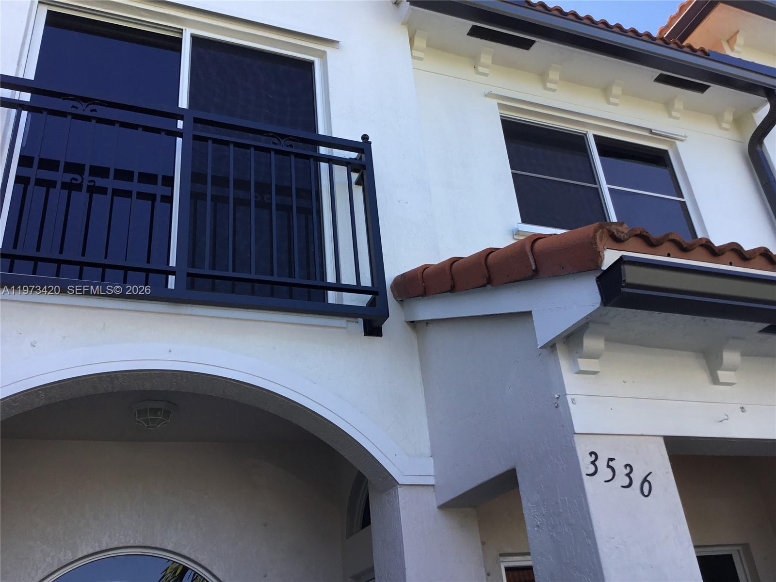 A two-story white stucco building features a black metal balcony and a tiled roof — LAUDERDALE LAKES, FL