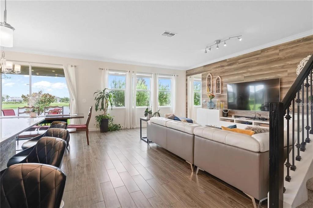 A living room with wood-look tile floors, a wood-paneled accent wall, and a large sectional sofa — 11819 IMAGINARY WAY, ORLANDO, FL