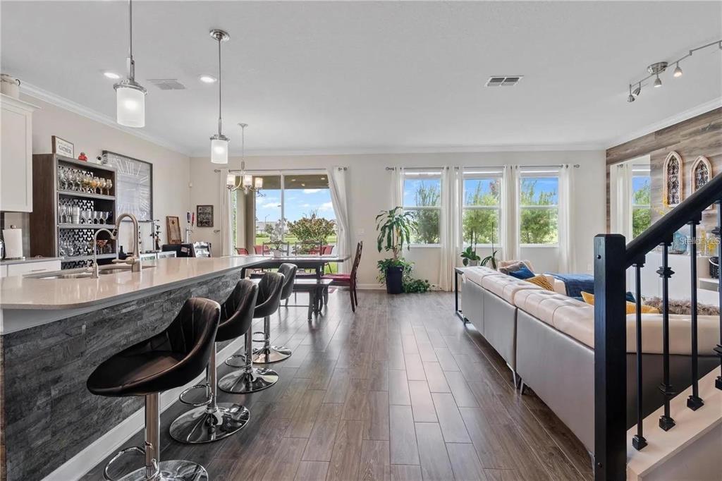 An open-concept kitchen and living area featuring a stone-faced island, bar stools, and wood flooring — 11819 IMAGINARY WAY, ORLANDO, FL