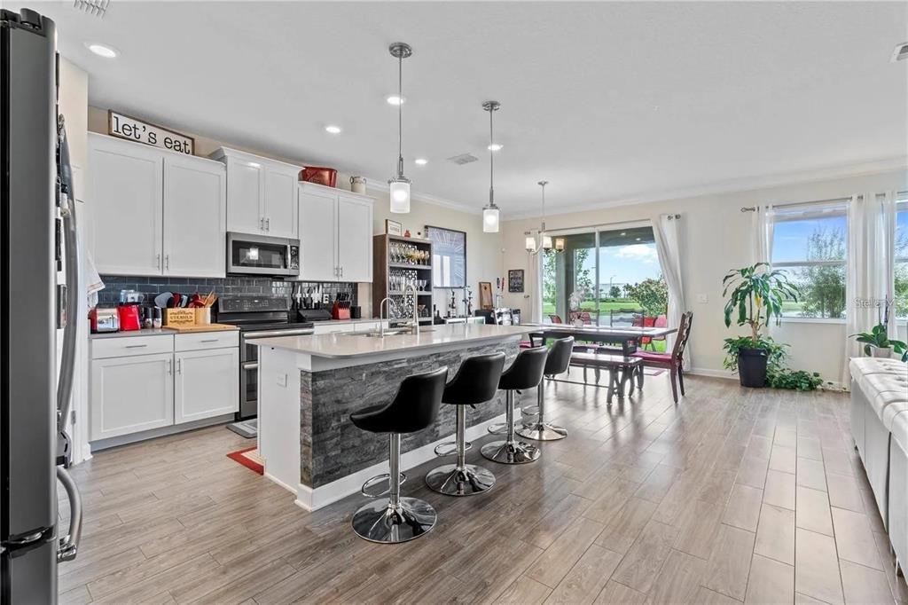 A kitchen with white cabinets, a stone-faced island with bar stools, and wood-look flooring — 11819 IMAGINARY WAY, ORLANDO, FL