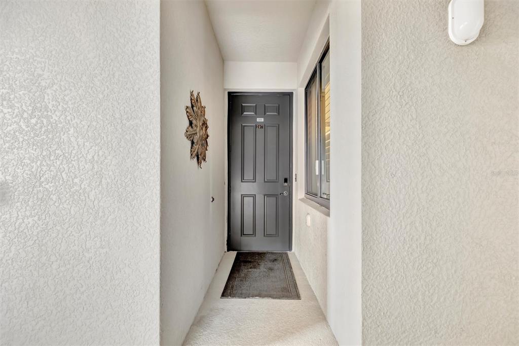 A dark gray front door with a number plate is centered in a small entryway — 17118 VARDON TERRACE UNIT 207, BRADENTON, FL