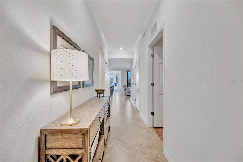 A hallway with tile flooring leads toward a living area with a wooden console table — 17118 VARDON TERRACE UNIT 207, BRADENTON, FL