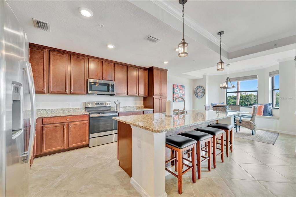 A kitchen with wood cabinets, granite countertops, stainless steel appliances, and a breakfast bar island — 17118 VARDON TERRACE UNIT 207, BRADENTON, FL