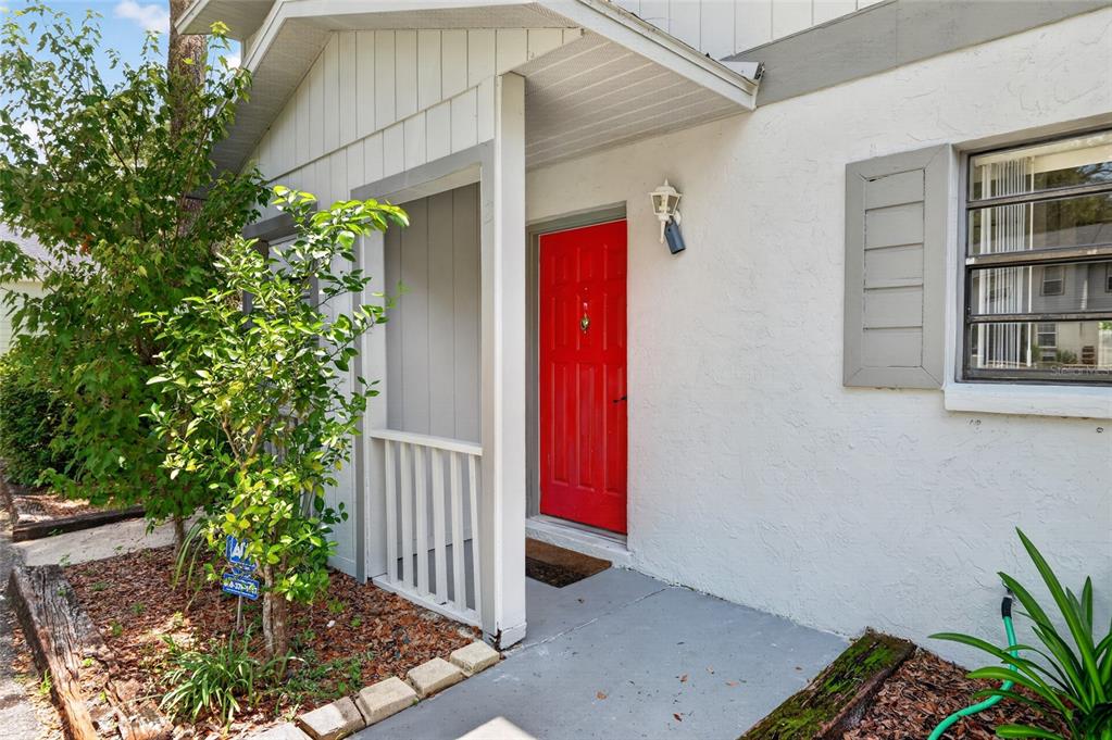 A bright red front door is set within a covered entryway of a white house — 4123 SW 15TH PLACE UNIT 2, GAINESVILLE, FL