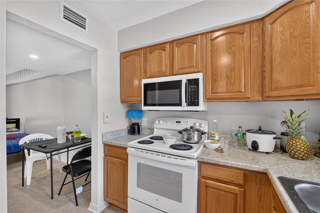 A kitchen with wood cabinets, white appliances, and granite-look countertops next to a dining area — 4123 SW 15TH PLACE UNIT 2, GAINESVILLE, FL