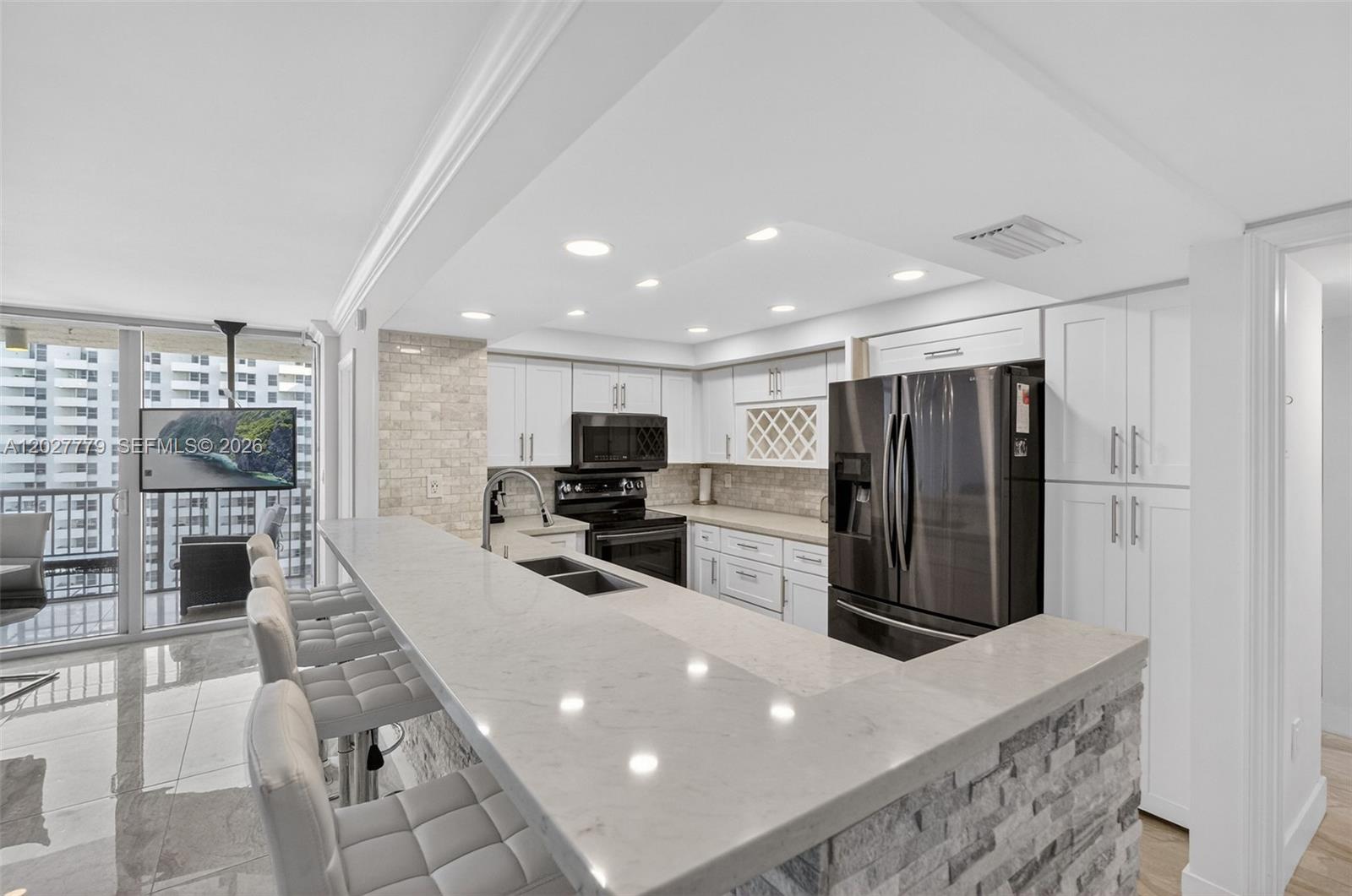 A modern kitchen features white cabinetry, stone countertops, a breakfast bar, and stainless steel appliances — 2655 Collins Ave # 1407, Miami Beach FL 33140, MIAMI BEACH, FL