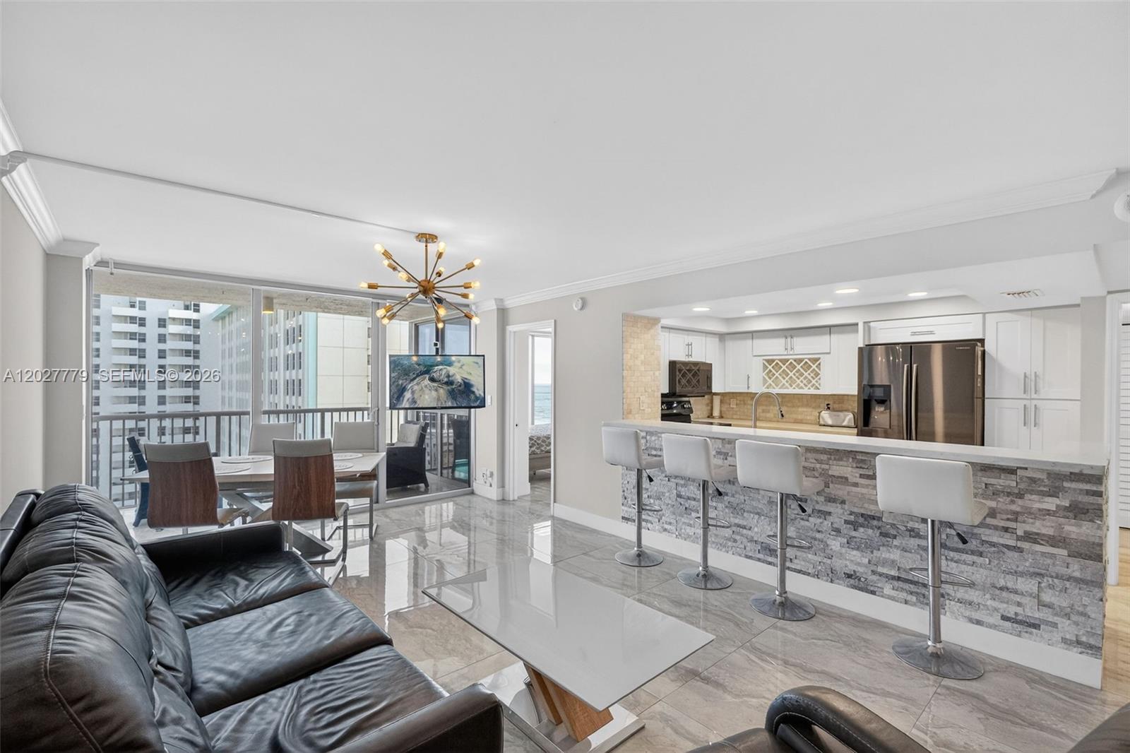 A modern open-concept living area features a kitchen with bar seating and a balcony view — 2655 Collins Ave # 1407, Miami Beach FL 33140, MIAMI BEACH, FL