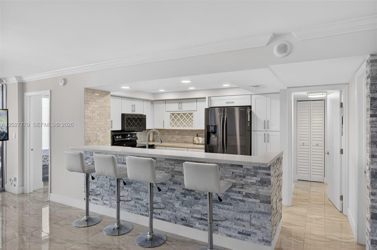 A kitchen features a stone-faced breakfast bar with four stools and white cabinetry — 2655 Collins Ave # 1407, Miami Beach FL 33140, MIAMI BEACH, FL