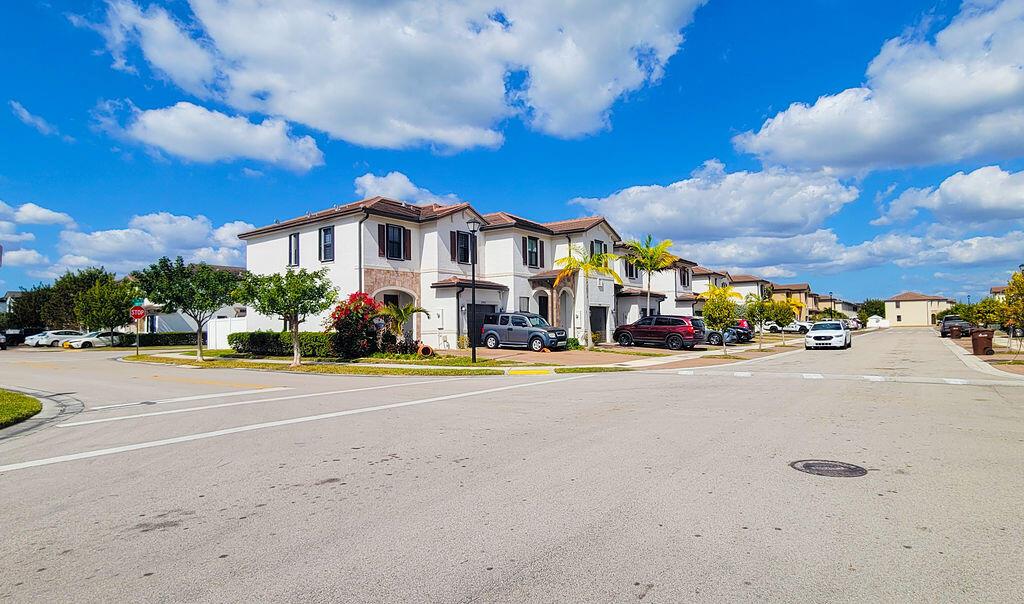 A street view of multi-story residential townhomes with driveways and palm trees under a blue sky — 10902 W 33rd Way, Hialeah FL 33018, HIALEAH, FL