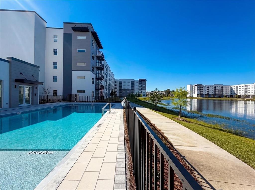 An outdoor swimming pool sits beside a modern apartment building and a small lake — 5587 MILLENIA PARK BLVD UNIT 515, ORLANDO, FL