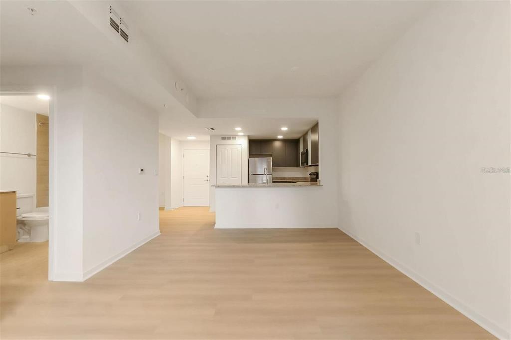 A bright, open-concept living area features light wood-look flooring and a kitchen with a breakfast bar — 5587 MILLENIA PARK BLVD UNIT 515, ORLANDO, FL