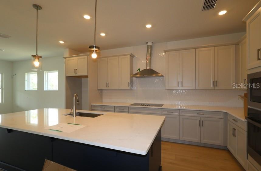 A modern kitchen features a large dark island, light gray cabinetry, and stainless steel appliances — 5681 LEAFLET TRAIL, MOUNT DORA, FL