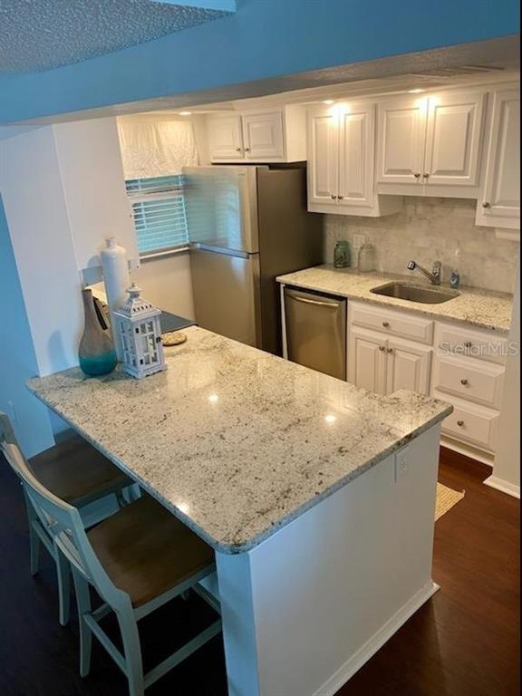A kitchen features white cabinets, granite countertops, stainless steel appliances, and a breakfast bar — 3235 GULF OF MEXICO DRIVE UNIT A302, LONGBOAT KEY, FL