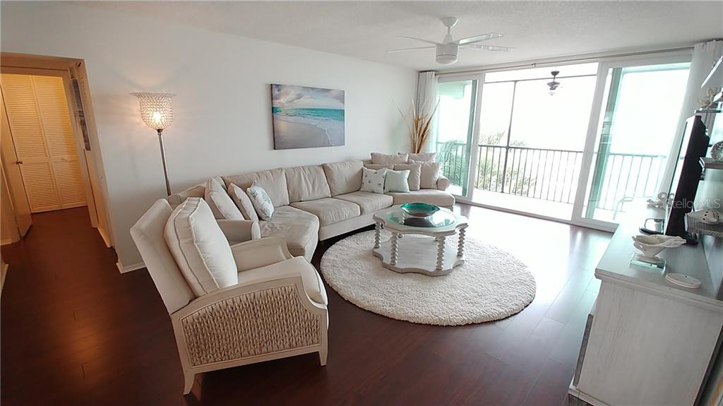 A living room features a beige sectional sofa, a round rug, and a glass-topped coffee table — 3235 GULF OF MEXICO DRIVE UNIT A302, LONGBOAT KEY, FL