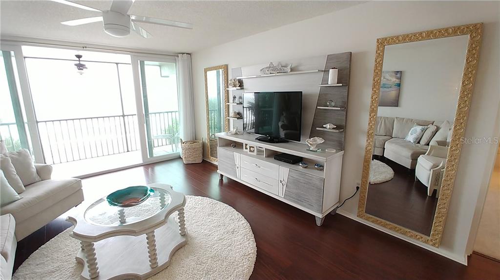 A living room features a white entertainment center, a large floor mirror, and a balcony view — 3235 GULF OF MEXICO DRIVE UNIT A302, LONGBOAT KEY, FL