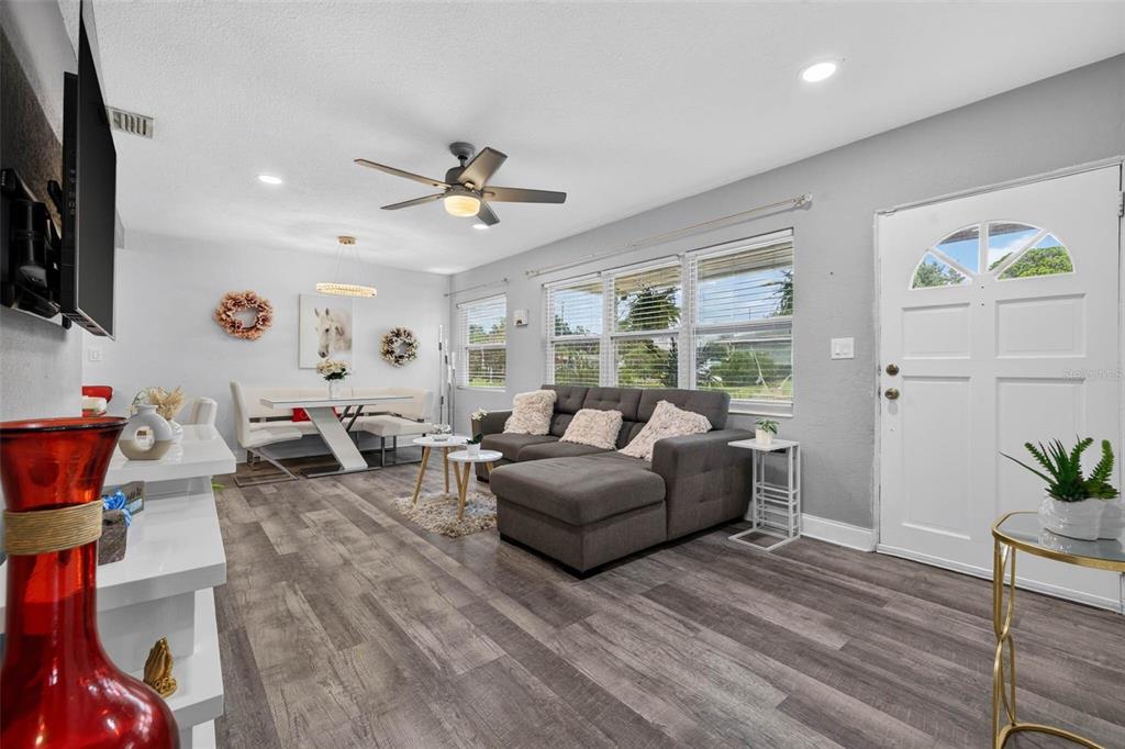 A living room with gray wood-look flooring, a gray sectional sofa, and a dining area — 3164 52ND WAY N, ST PETERSBURG, FL