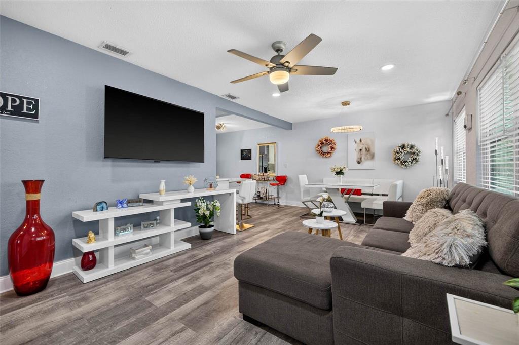 A living room features a grey sectional sofa, a wall-mounted television, and wood-look flooring — 3164 52ND WAY N, ST PETERSBURG, FL